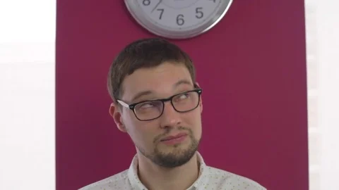 Close-up man with glasses stands on the background with a clock. The office has Stock Footage 74096464