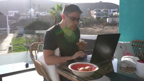 Close-up of a man with glasses working on his laptop and eating sliced bread Stock Footage 155825777