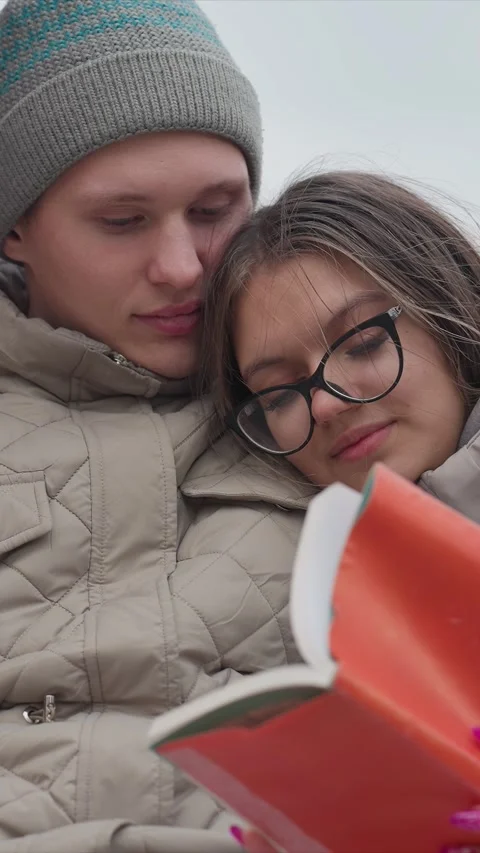 Close up of man in gray knit hat and woman with glasses reading orange book Stock Footage 345543952