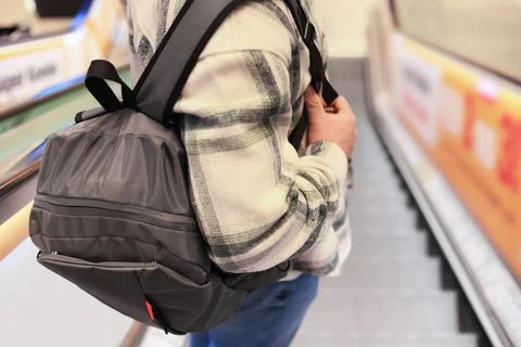 Close up of man with grey backpack standing on escalator. Person wearing pl.. Stock Photos