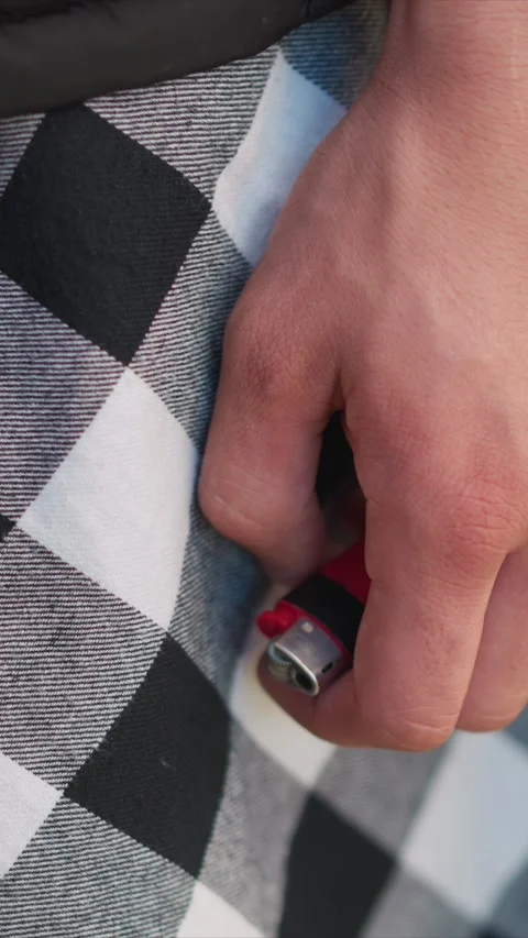 Close up of man hand holding red lighter against checkered patterned textile Stock Footage 345059245