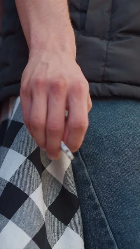 Close up of man hand holding unlit cigarette near checkered and denim fabrics in Stock Footage 345059569