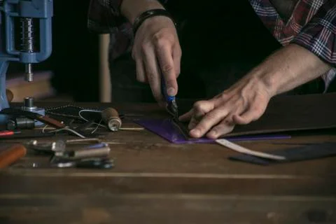 Close up of man hand leather maker working on wooden table with tools Stock Photos