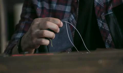 Close up of man hand leather maker holding wallet of blue color and sewing Stock Photos