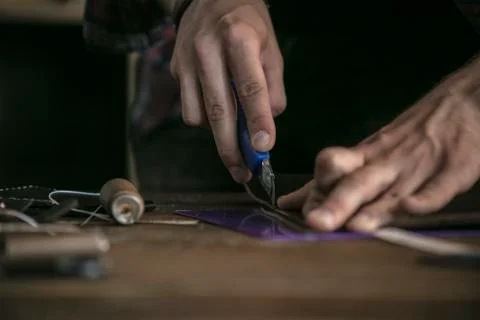 Close up of man hand leather worker cuts off extra piece of leather with knife Stock Photos