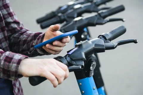 Close up of man hand using mobile app for rental electric scooter. Stock Photos