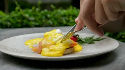 Close-up man hands with fork and knife cuts eggs benedict in outdoor restaurant Video stock 163138475