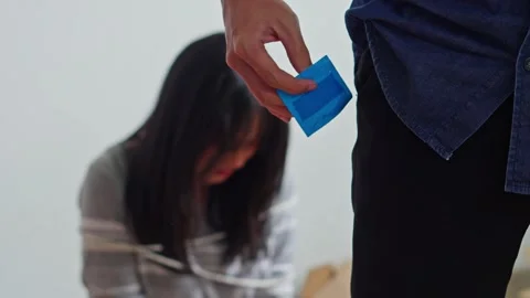Close-up of man hands holding condom packet with blurred tied-up woman in Stock Footage 333508826
