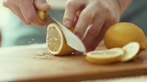 Close up of man hands slicing fresh lemon on wooden board near glass of water, h Stock Footage 332672393