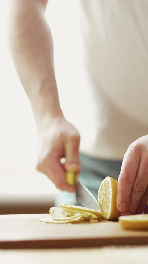 Close up of man hands slicing fresh lemon on wooden board near glass of water, h Stock Footage 332680287
