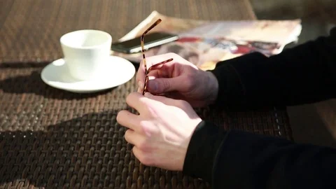 Close-up Man Hands with Sunglasses, cup of Coffee, glossy Magazine on Cafe Table Stock Footage
