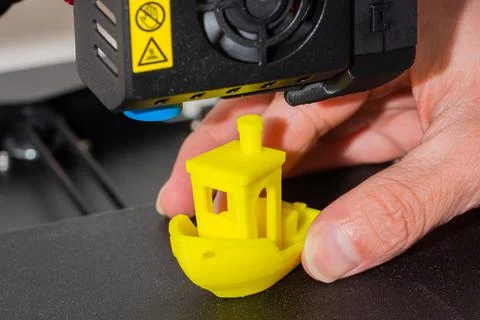 Close-up of man hands taking finished 3D printed model of yellow PLA ship Stock Photos