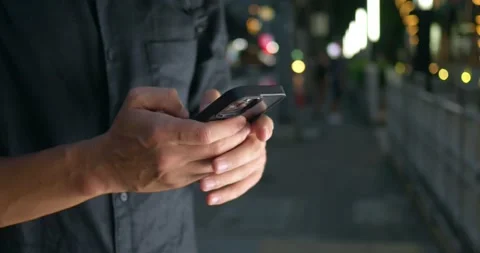 Close up man hands typing text message on mobile phone at night city street Stock Footage 252377642