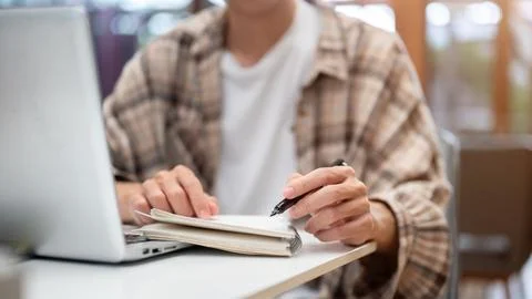 Close up of a man hands writing in notebook with a fountain pen over laptop.. Stock Photos