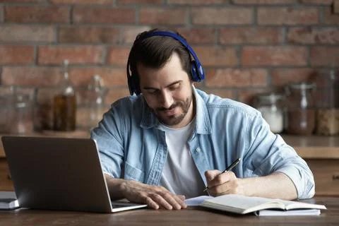 Close up man in headphones taking notes, using laptop Stock Photos