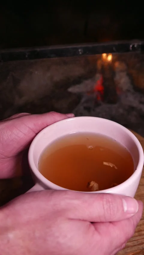 Close-up: man holding and moving a big teacup by the fireplace (slow zoom out) Stock Footage 336825436