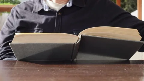 Close-up of a man holding and reading an old book on a wooden table Stock Footage 229840590