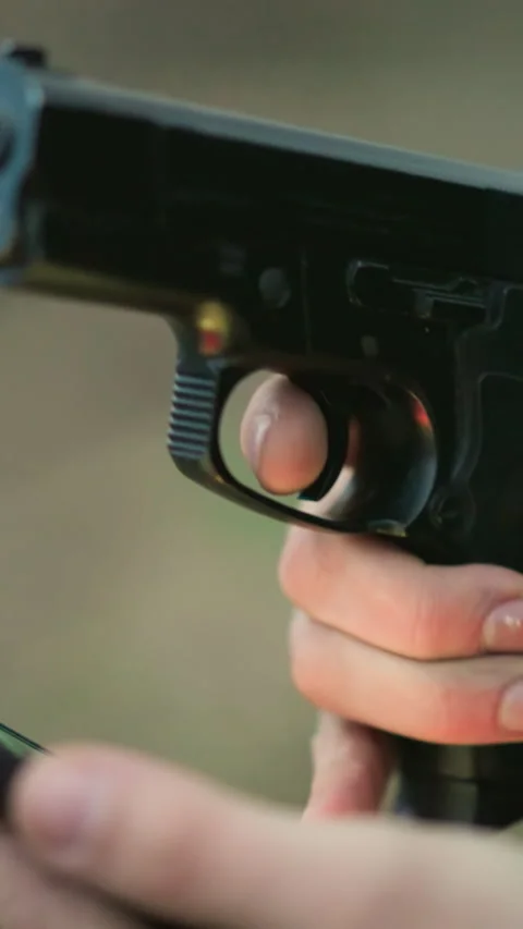 Close-Up of Man Holding Cell Phone and Gun with Finger on Trigger Stock Footage 316502193