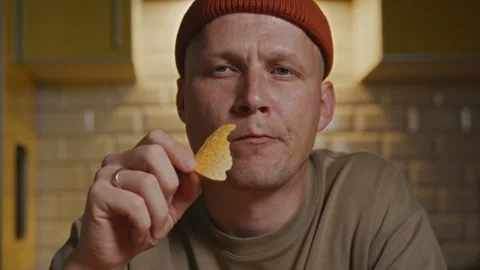 Close up of man holding chip in calm evening kitchen ritual Stock Footage 317991869