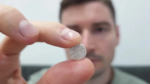 Close-up of a man holding a pill between fingers with focus on the tablet Stock Footage 284042273