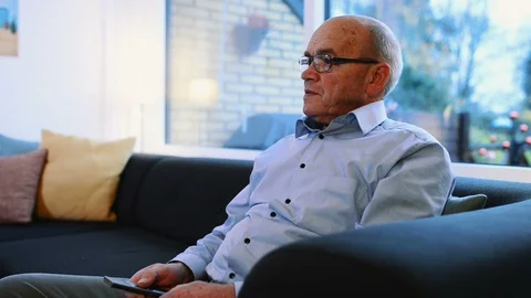 Close up of man holding remote as he watches television in his living room Stock Footage 99013019