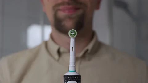 A close-up of a man holding a sleek black electric toothbrush, turning it on and Stock Footage 321426464