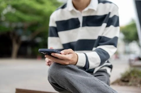 Close up of a man holding smartphone while sitting cross legged on a wooden.. Stock Photos