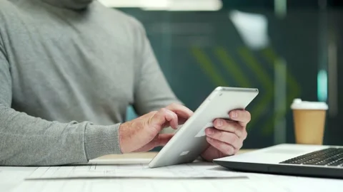 Close up. Man holding a tablet while sitting at a desk at a workplace in a mode Stock Footage 232576981