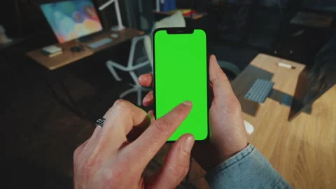 Close up man holds and scrolling phone with a vertical green screen in a dark Stock Footage 238744110