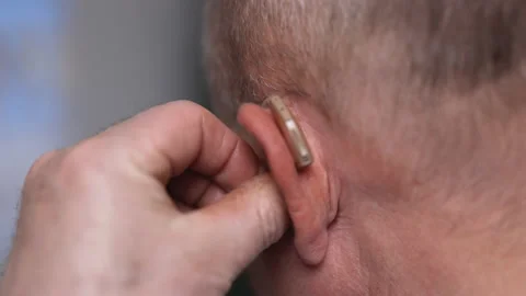 Close up of man inserts a hearing aid into her ear. Old man using hearing aids 動画素材 194746293