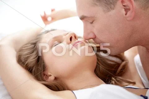 Close-up of a man kissing his girlfriend lying in bed Stock Photos