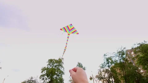 Close-up, man launching a flying, bright, colorful, rainbow kite into the blue Stock Footage 132326714