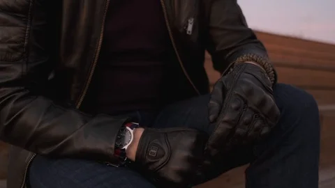 Close-up, a Man in a leather jacket and gloves looking at his watch. Stockbeeldmateriaal 121760284