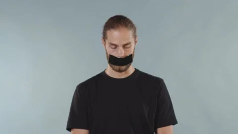Close up man looking at camera serious and tearing tape from her mouth on grey Stock Footage 133638197