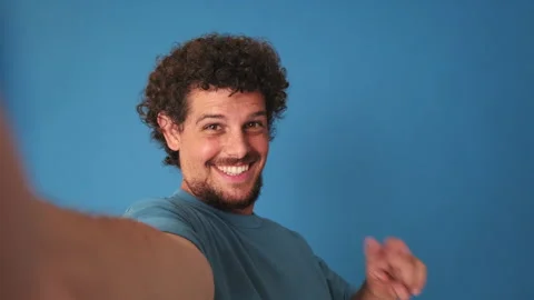 Close-up of man looking at camera, taking selfie, victory sign, isolated on blue Stock Footage 250841086