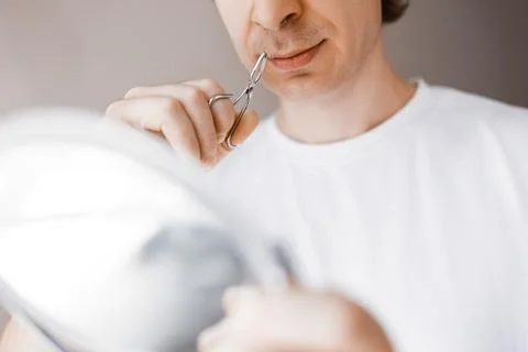 Close-up of a man looking in a mirror using tweezers for nose hair removal... Stock Photos