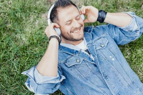 Close up of man lying on green grass and listening to music on headphones. Stock Photos