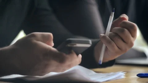 Close-up a Man making Notes with a Pen, Paper and Mobile Smart Phone in Hands Stock Footage 95636422