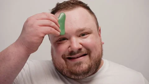 Close-up of a man massaging his face with gua sha on a white background Stock Footage 237549334