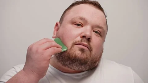 Close-up of a man massaging his face with gua sha on a white background Видео 237549424