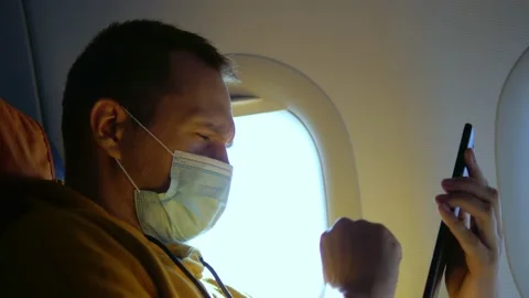 Close-up of a man in a medical mask using a smartphone on an airplane Stock Footage 139987432