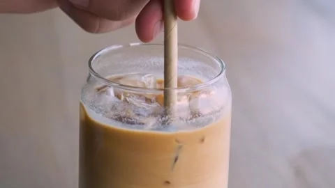 Close up of man mixing iced latte in a glass with a straw on cafe table. Cold Stock Footage 249663142