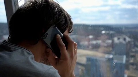 Close-up of a man near a window on a sunny morning who speaks by mobile phone Stock Footage 105799790
