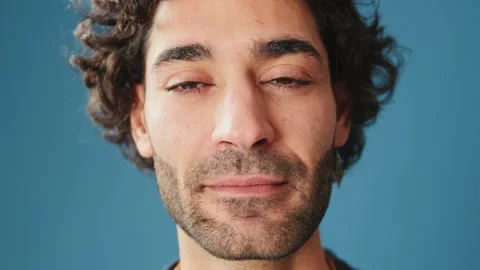 Close-up, man opens his eyes smiling and looking at camera isolated on blue Stock Footage 254913192
