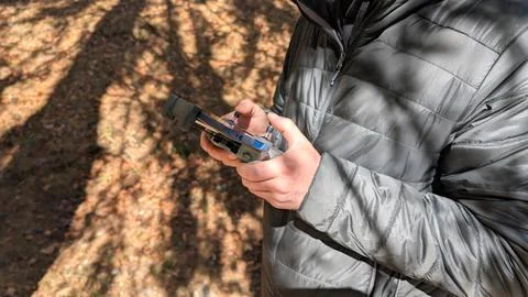 Close up of man operating drone controller with smartphone in forest park Foto stock