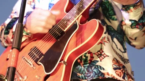 A close-up of a man in a patterned shirt plays a red electric guitar during a Stock Footage 200795660