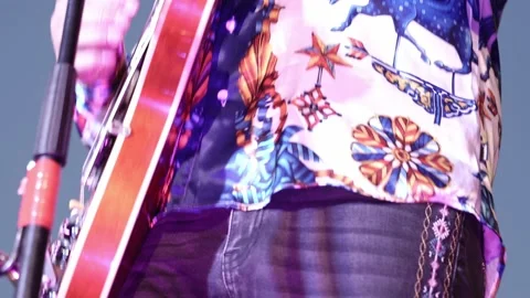 A close-up of a man in a patterned shirt plays a red electric guitar during a Stock Footage 200795683