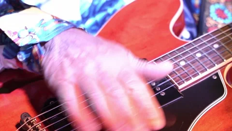 A close-up of a man in a patterned shirt plays a red electric guitar during a Stock Footage 200795735