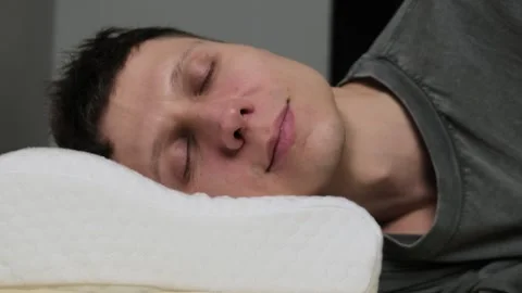 Close-up of a man peacefully sleeping on a memory foam pillow, showing relaxed Stock Footage 300772107