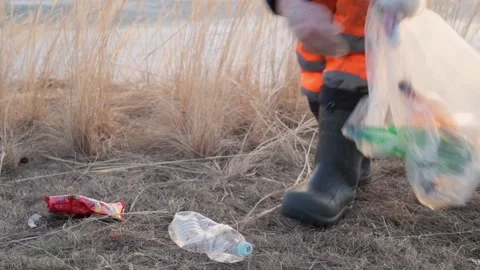 Close-up of a man picking up trash and plastic bottles on the shore of a lake. Stock Footage 238530115